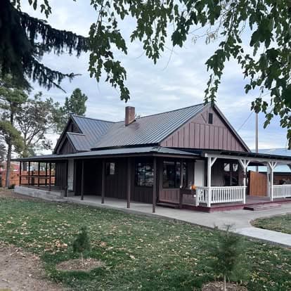 Charming brown house with a metal roof, porch, and surrounding greenery. Ideal for family gatherings.