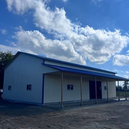 Newly constructed metal building with blue roof under a sunny sky and clouds.
