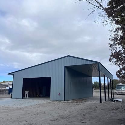 Modern blue metal building with open canopy and gravel surroundings under a cloudy sky.