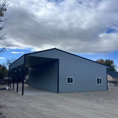 Modern steel building structure with large open space and gray exterior against cloudy sky.