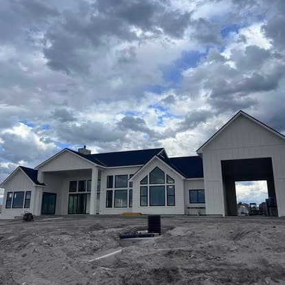 Modern white house with large windows under a cloudy sky, surrounded by construction site.