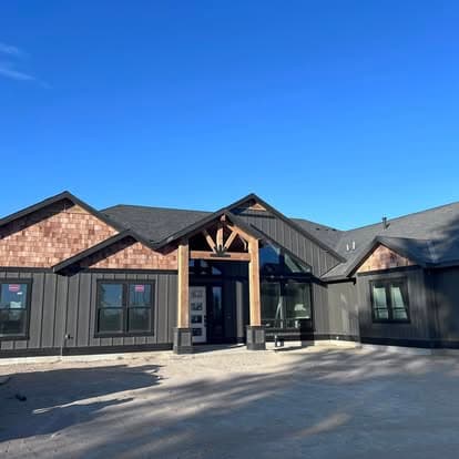 Modern black exterior home with wooden accents under a blue sky.
