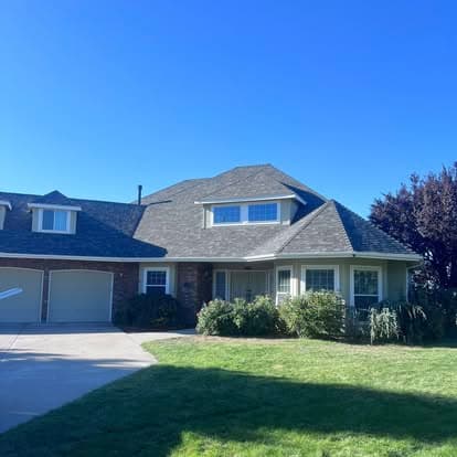 Family home with a gable roof, green lawn, and landscaped front yard under a clear blue sky.